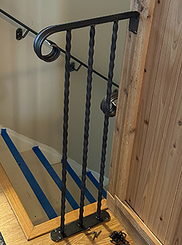 Stair pickets with twisted iron balusters installed on wood staircase railing